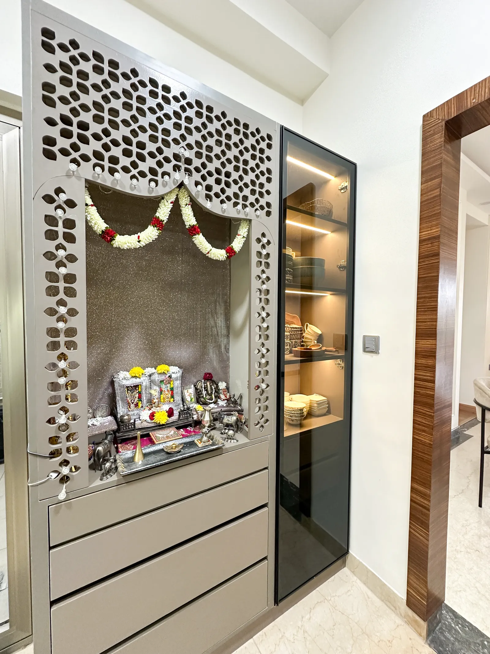 Pooja unit with jaali screen panel and lit glass cabinet — Somani's Residence